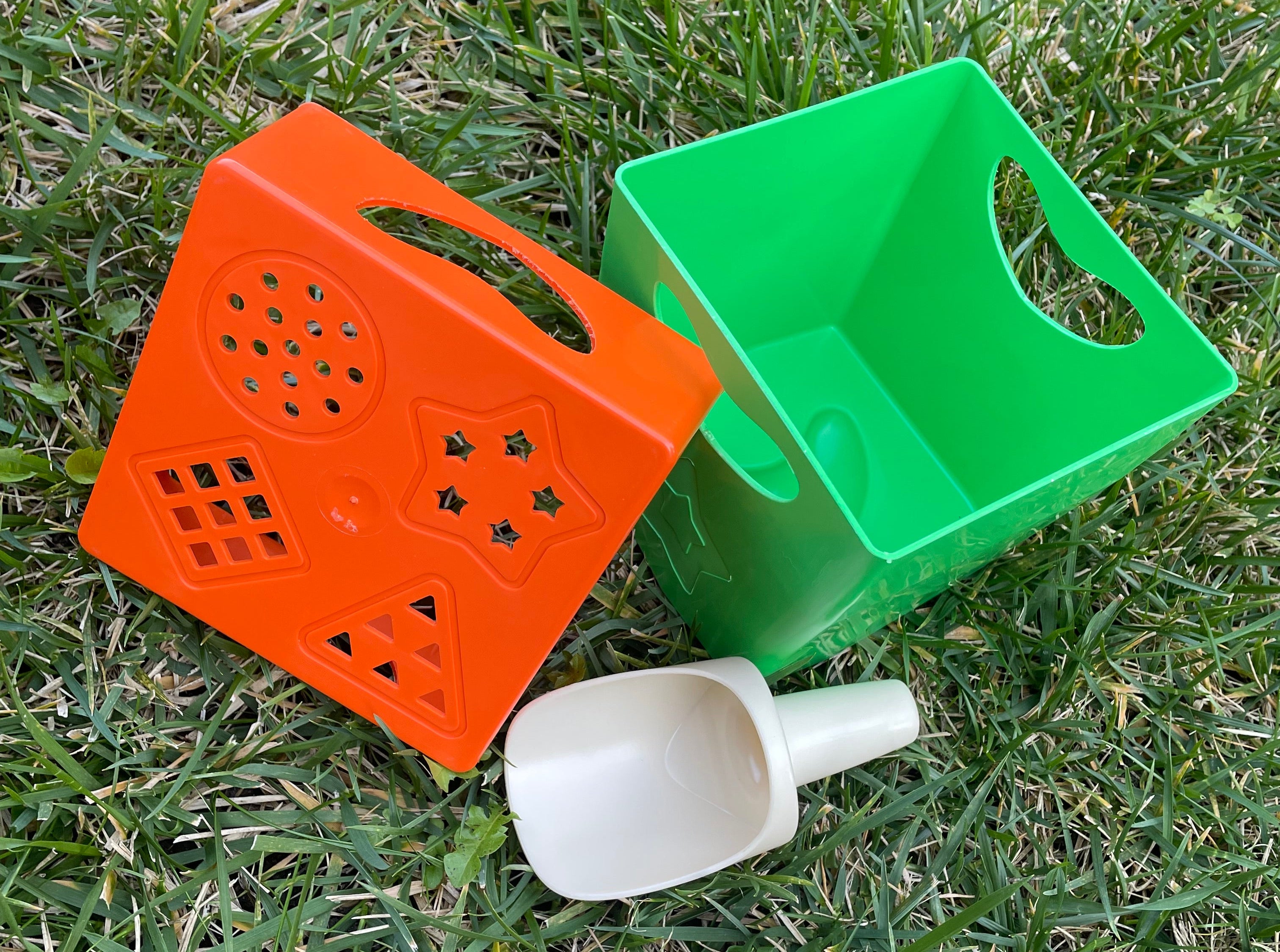 Green and orange plastic containers with a white scoop on grass
